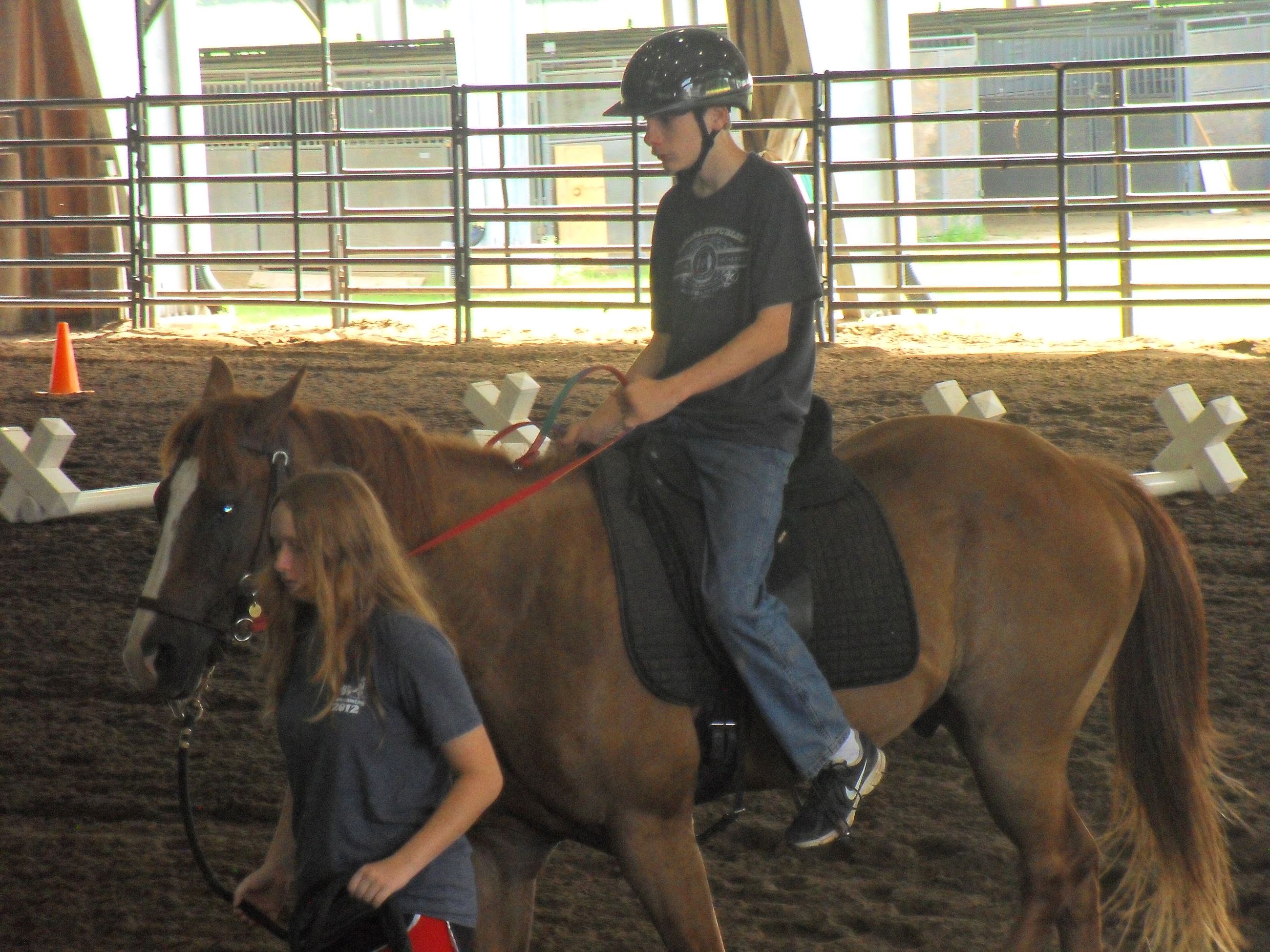 Child riding a horse around the arena with woman walking it