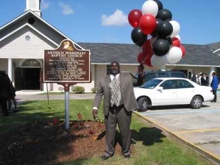 Pastor Holding balloons in front of the sign