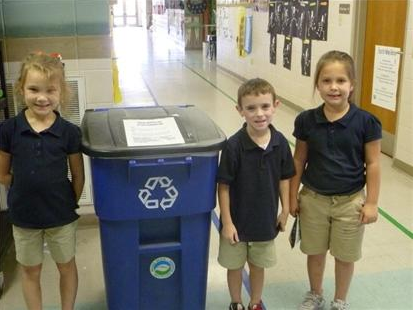 Three children pose next to recycling container